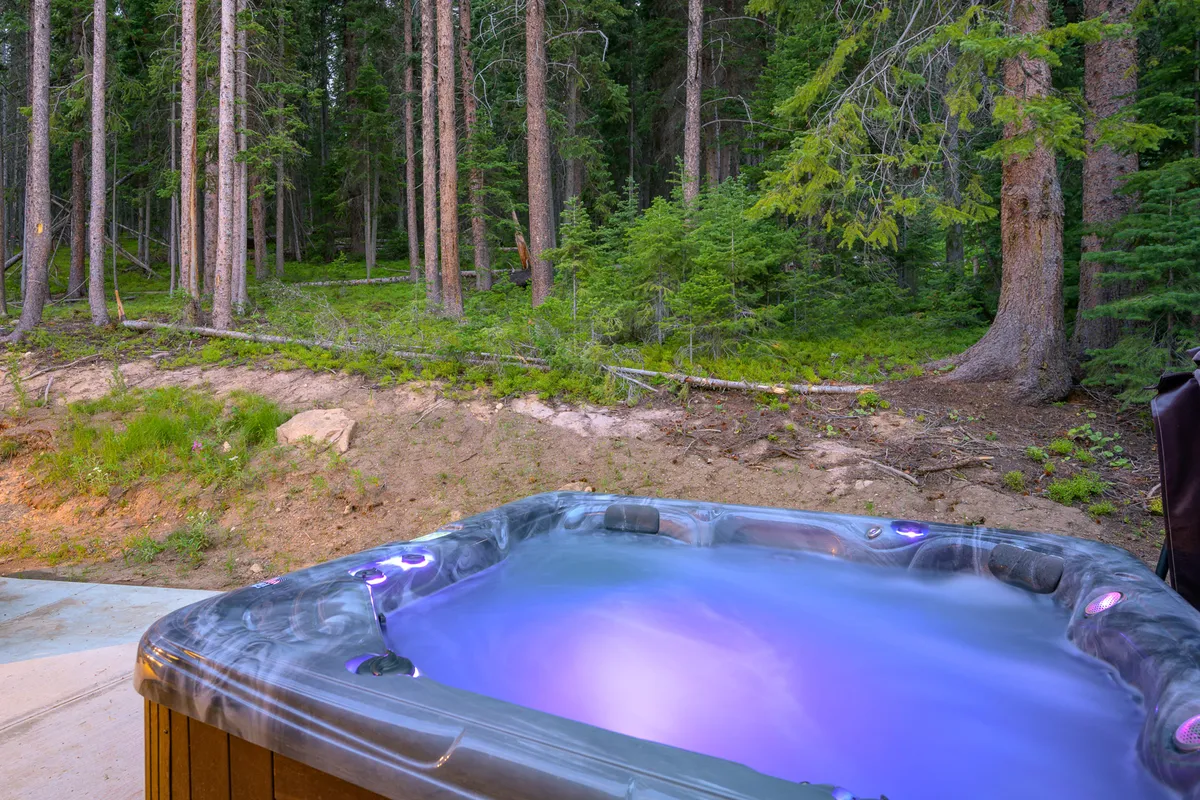 A secluded outdoor hot tub surrounded by a tranquil forest setting, with ambient lighting that welcomes guests to relax under the open sky. The scene invites stargazing and soaking after an adventurous day.