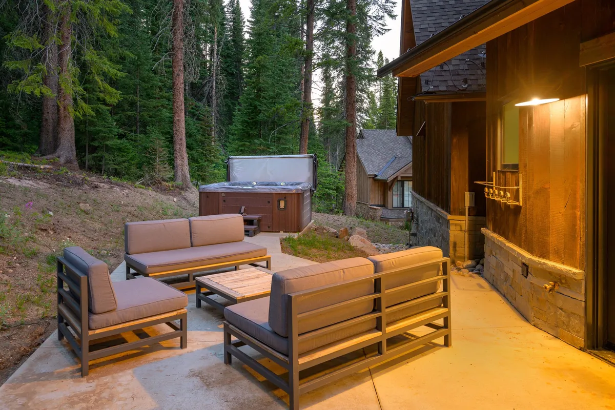 This inviting exterior photo features an outdoor seating area nestled among trees, with a hot tub as a focal point. The tranquil setting suggests a space for relaxing after a day of adventure, stargazing from the hot tub, or enjoying morning coffee surrounded by nature.