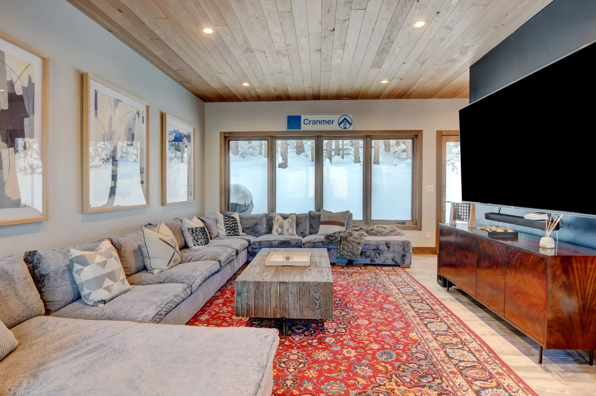 This image features a large sectional sofa positioned in front of a TV unit with a television. The space is accentuated with artwork on the walls and a wooden coffee table, exuding a welcoming and comfortable environment ideal for lounging and entertainment. The setup is perfect for movie nights and group activities.