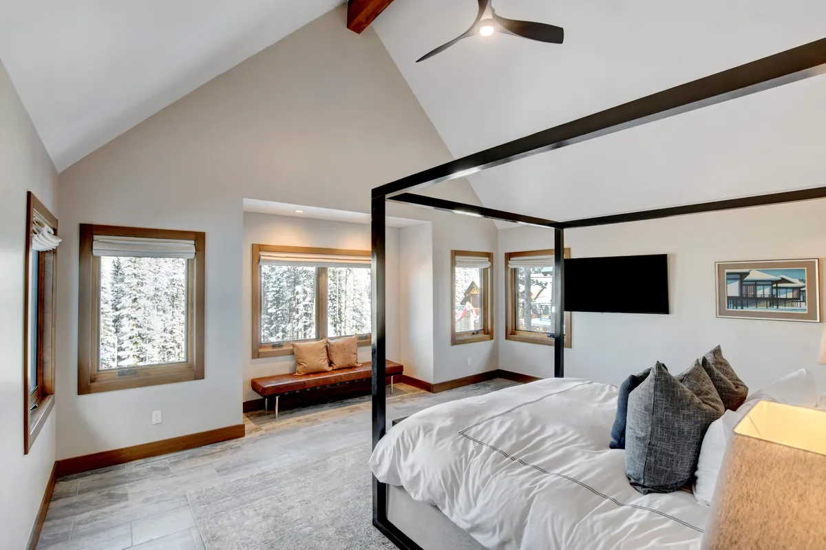 A serene bedroom featuring a canopy bed with soft bedding and large windows that frame picturesque mountain views. The wooden bench and wall art add cozy, personal touches, while natural light fills the space, creating a tranquil environment for relaxation and restful nights.