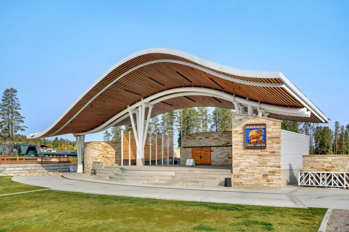 An outdoor amphitheater with a curved roof structure, stone facade, and stage area set against a scenic backdrop. The space is designed for community events, concerts, and gatherings, embodying the festive spirit of downtown Winter Park.