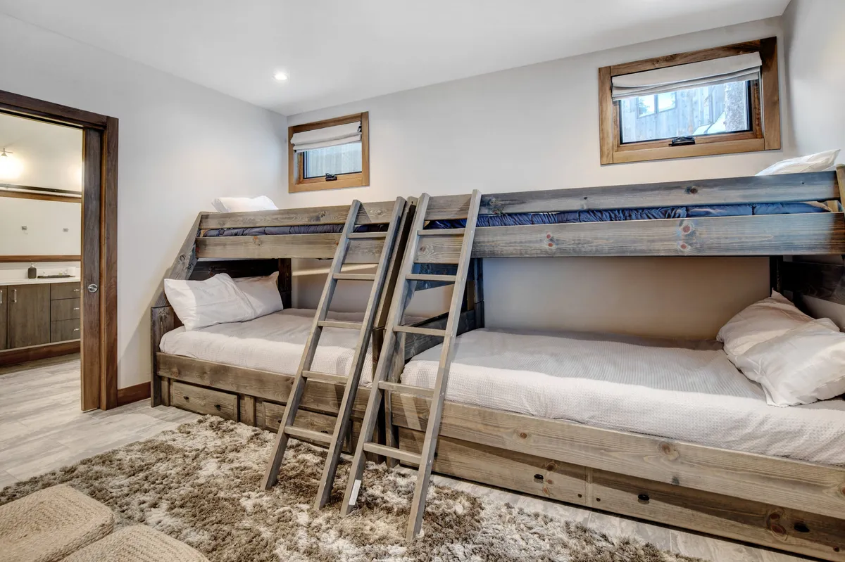 A welcoming bunk room with wooden ladder and textured rug, designed for group or family stays. Multiple bunk beds, windows with natural light, and playful decor create a fun and inviting space perfect for children or friends.