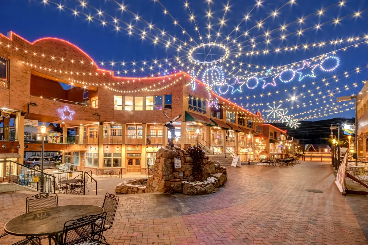 A lively downtown scene with string lights overhead, decorative stars, a stone fountain, and inviting seating areas. The atmosphere suggests festive socializing, evening strolls, shopping, and dining—hallmarks of a bustling, welcoming downtown.