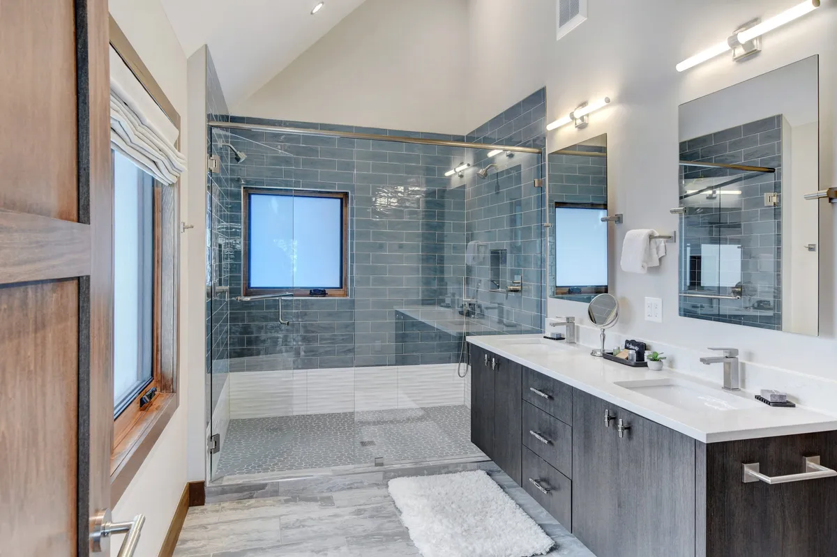 A spa-inspired bathroom featuring large mirrors, a glass shower enclosure, dual sinks, and calming blue tile walls. The space feels bright and refreshing, inviting guests to enjoy self-care routines and rejuvenating showers.